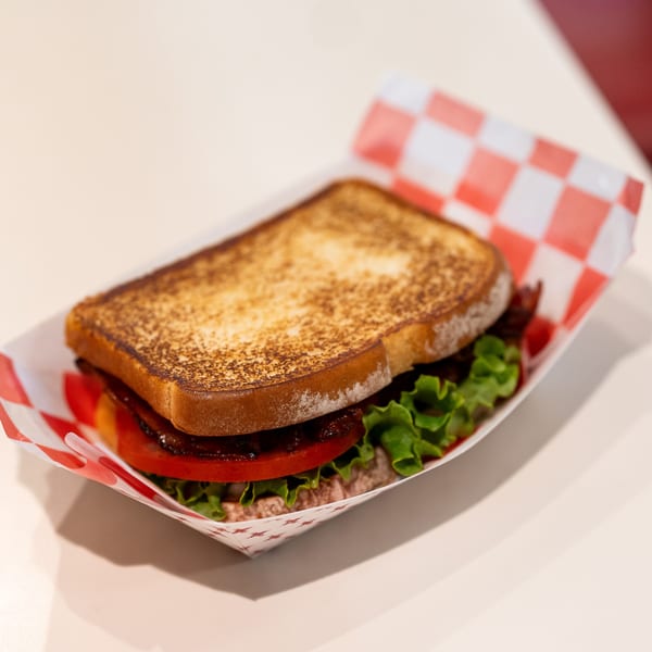 A DickieJo's BLT sandwich with toasted bread, bacon, lettuce, and tomato in a paper tray.