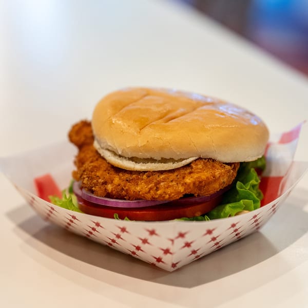 DickieJo's crispy chicken sandwich with lettuce, tomato, and red onion in a paper tray.