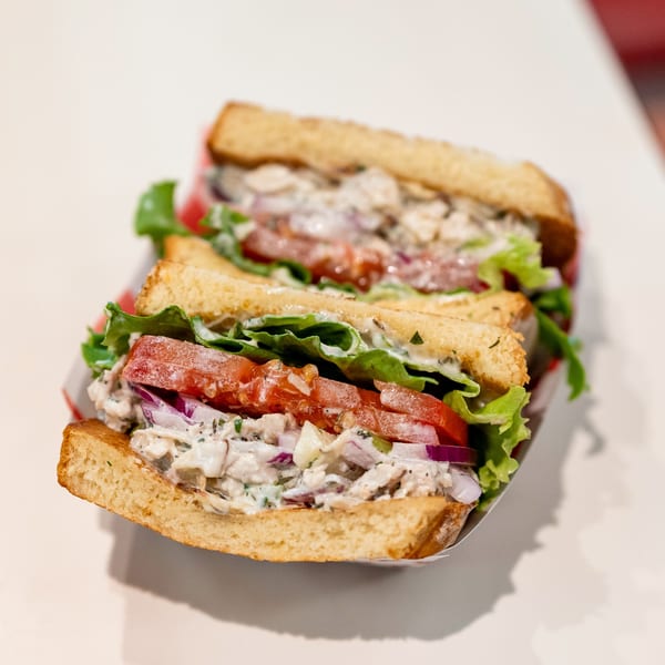 Two halves of a chicken salad sandwich with lettuce, tomato, and red onion on toasted bread.