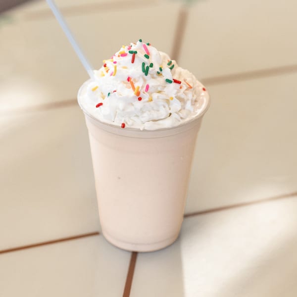 DickieJo's vanilla milkshake topped with whipped cream and colorful sprinkles, with a straw.