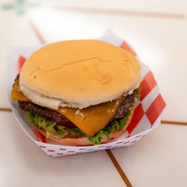 A DickieJo's cheeseburger with lettuce and tomato in a red and white checkered paper tray.