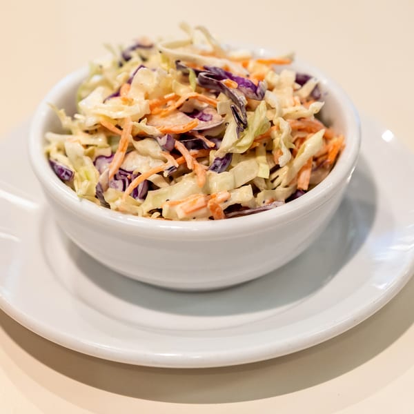 A white bowl of DickieJo's Burgers coleslaw, with shredded cabbage and carrots in a creamy dressing.