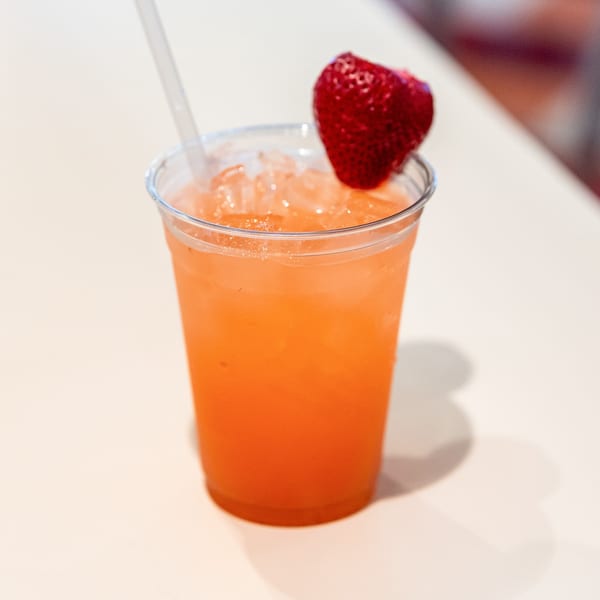 A vibrant orange drink with ice, a straw, and a fresh strawberry garnish in a clear cup.
