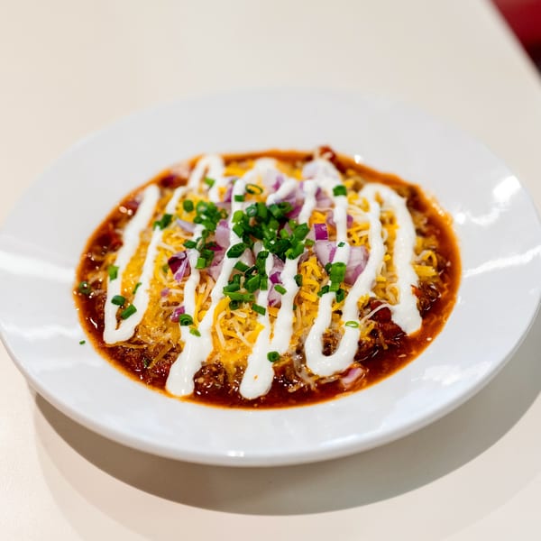 A bowl of DickieJo's chili, topped with shredded cheese, sour cream, red onions, and chives.