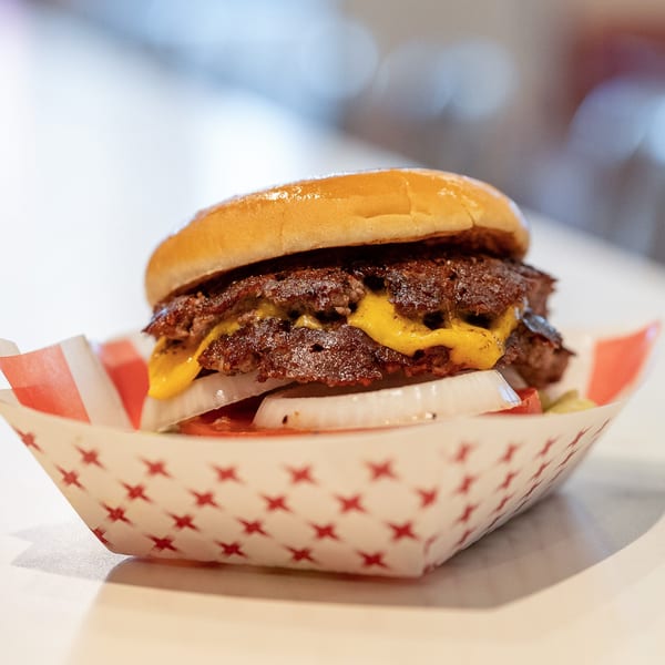 DickieJo's double cheeseburger with melted cheese, onions, and tomatoes in a red and white paper tray.